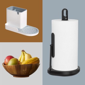 A utensil holder with a drainage base, a wooden fruit bowl holding bananas and mangoes, and a standing paper towel holder with a sleek design.
