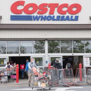 Shoppers push carts outside a Costco Wholesale entrance, with stacked shopping carts and the store's branded sign above.