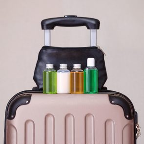 Bottles sit atop a hard-shell suitcase with an extended black handle, against a plain background.