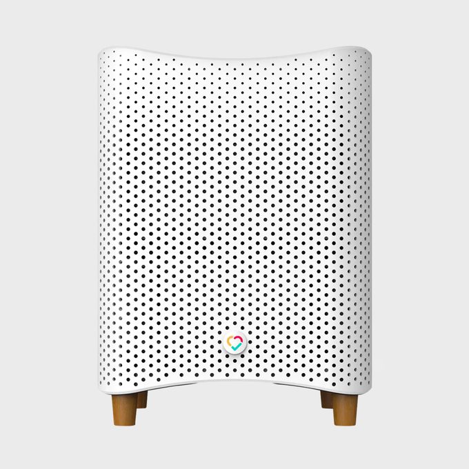 White air purifier standing upright; features perforated holes and wooden legs; positioned against a plain gray background.