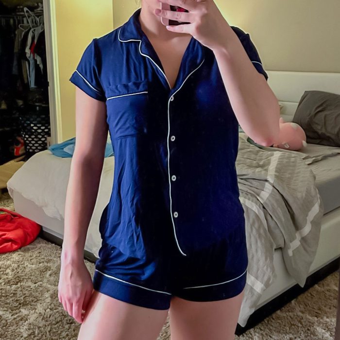 Person wearing blue pajamas takes a mirror selfie in a bedroom with an unmade bed and open closet in the background.