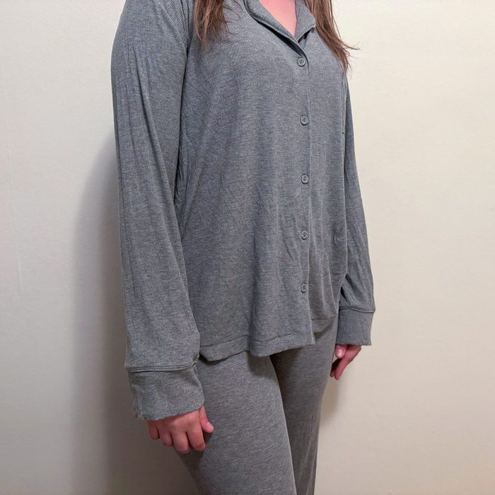 Gray button-up pajamas hang on a standing person against a plain wall.