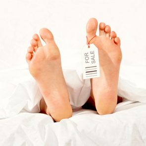 Feet lie still under white sheets, tagged 