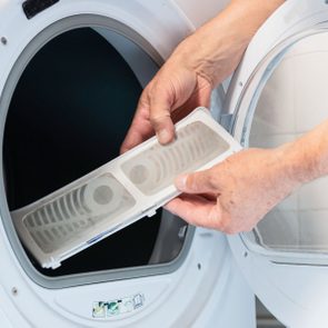 Hands remove lint filter from open dryer door, inside a laundry room setting.