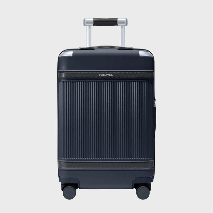 Suitcase stands on four wheels, featuring ridged texture and telescopic handle, set against a plain background. Text reads 