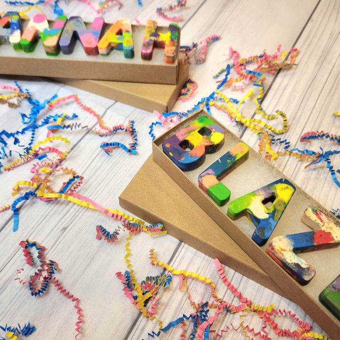 Colorful block letters rest on cardboard, surrounded by scattered multicolored shredded paper on a light wooden surface.
