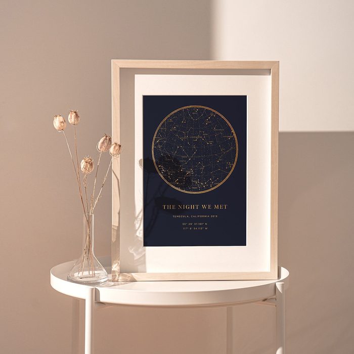 Framed star map resting on a table, displaying a constellation design. Nearby, dried flowers stand in a vase, creating a decorative setting.
