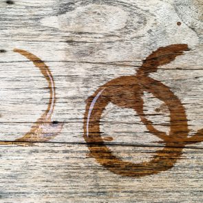 Brown liquid rings stain a textured, light wooden surface, suggesting spilled beverages on a table.