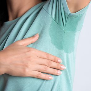 A hand holds a green shirt with a noticeable sweat stain in an indoor setting.