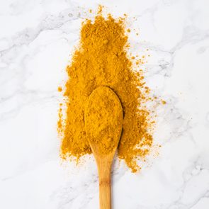 A wooden spoon holds turmeric powder, surrounded by more spilled powder, on a white marble surface.