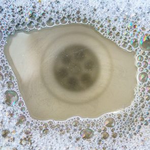 Foamy bubbles circle a drain in a sink, reflecting colorful light, creating a vibrant, soapy pattern.