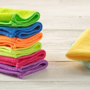 Colorful microfiber cloths stacked neatly on a white wooden surface, displaying vibrant shades of green, blue, orange, yellow, pink, and purple.