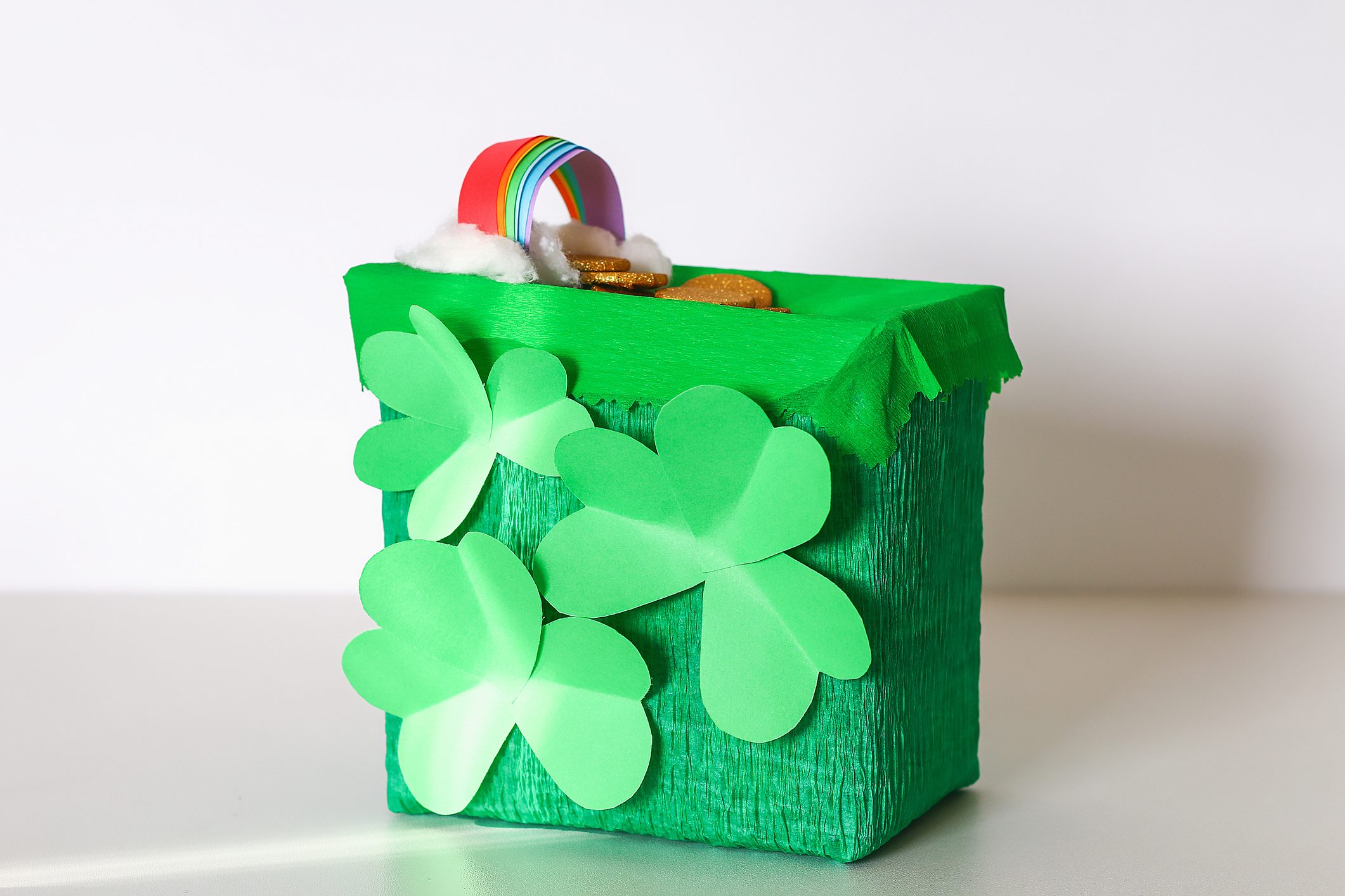 DIY leprechaun trap with gold coins, rainbow and green ladder St Patricks Day background.