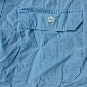 A light blue fabric pocket, secured with a white button, is displayed against a matching wrinkled background.