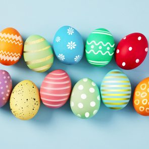 Colorful decorated eggs lie in a row on a light blue background, featuring various patterns like stripes, dots, and flowers.