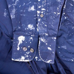 Shirt with paint splatters displayed on a crumpled fabric background.