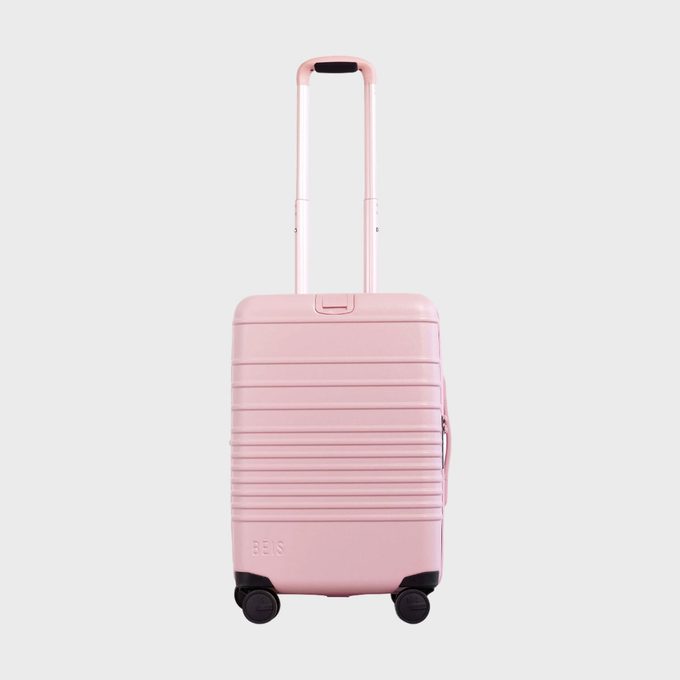 Pink suitcase stands upright, handle extended, on a plain white background.