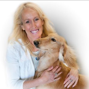 A woman smiles while holding a tan dog, both in a soft-focus setting with a white background.