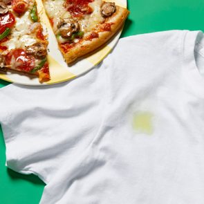 White shirt stained with pizza grease rests beside a plate of pizza slices on a green surface.