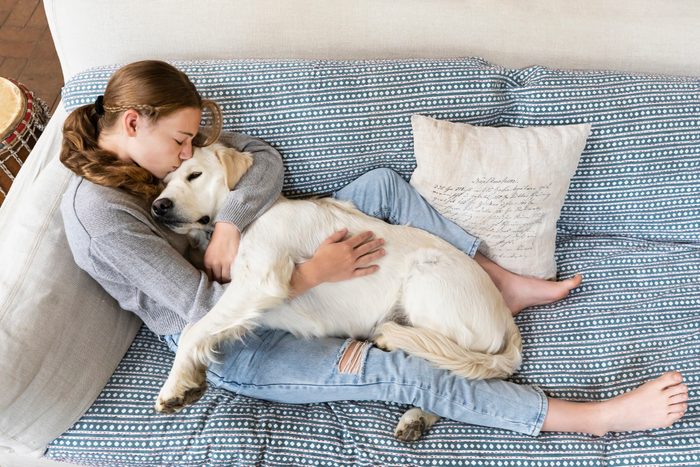 Girl (14-15) embracing English Cream Golden Retriever on sofa