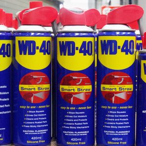 Cans of WD-40 stand on a shelf, featuring red smart straw caps; labeled to stop squeaks, drive out moisture, and clean.