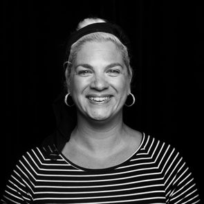 Woman smiling, wearing hoop earrings and striped shirt, stands against a dark background.