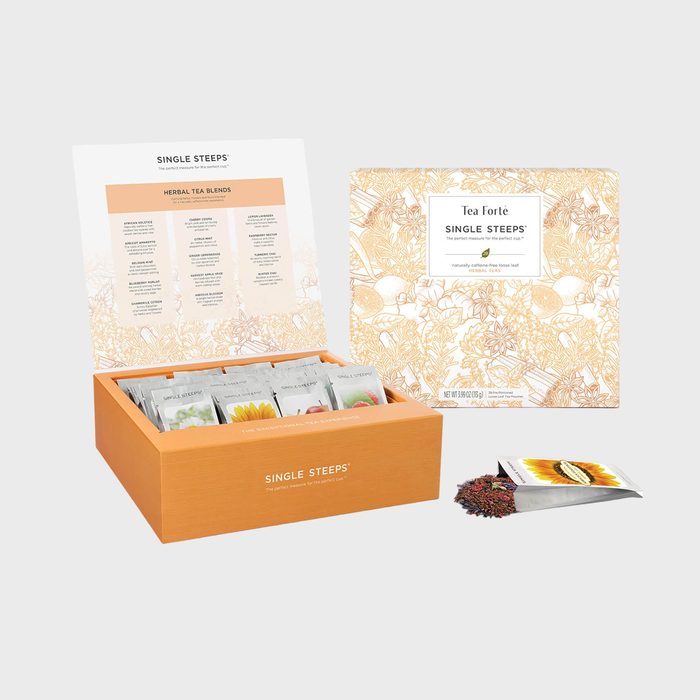 Box displays assorted tea packets with open lid showing flavor list, surrounded by ornate packaging, accompanied by a spilled packet of loose tea.