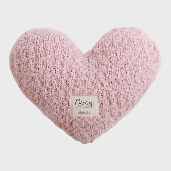 Pink heart-shaped pillow, resting on a plain background; textured surface, with a label reading 