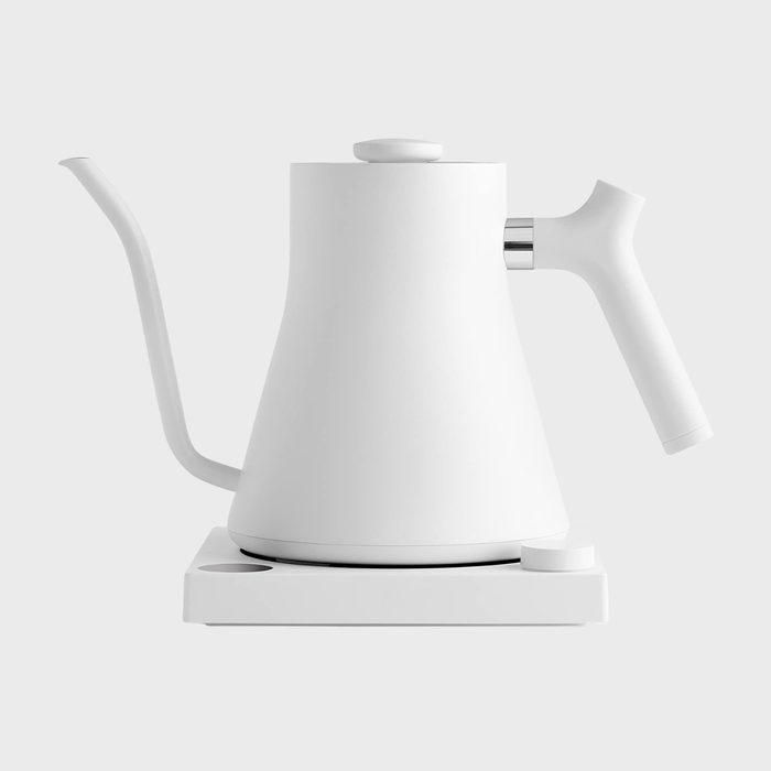 White electric kettle sitting on a base, featuring a long gooseneck spout, in a minimalist setting.