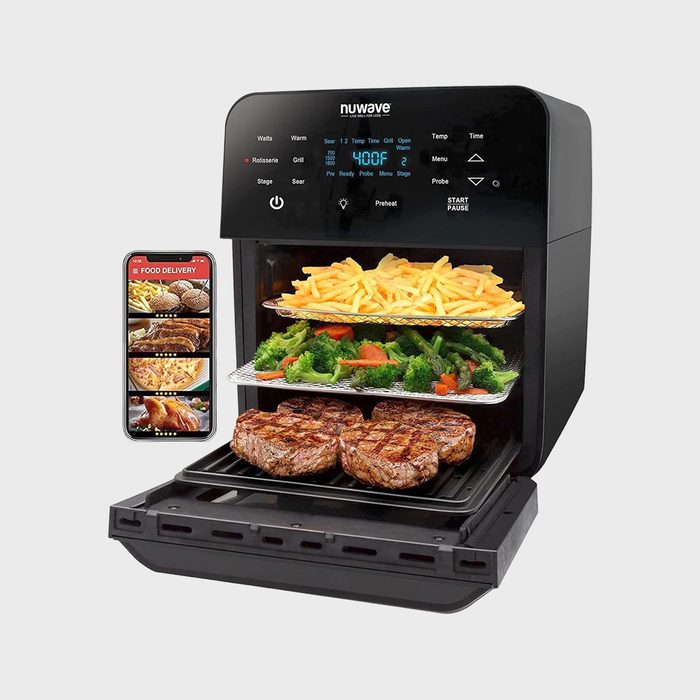 Air fryer cooks steak, vegetables, and fries on trays; screen displays temperature as 400Â°F. A smartphone with a food delivery app is beside it.