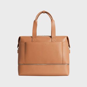 Tan leather duffel bag, standing with visible handles, and a zippered bottom compartment, against a plain white background.