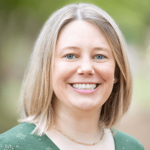 A person smiles warmly, looking directly at the camera, with a blurred, green outdoor background.