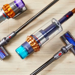 Vacuum cleaners lay on a light wooden floor, showcasing cylindrical canisters, colorful brush heads, and sleek handles in an arranged display.
