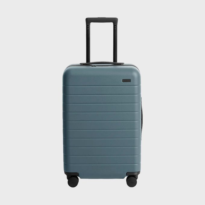 Suitcase stands upright, handle extended, on white background. Four wheels support it. 