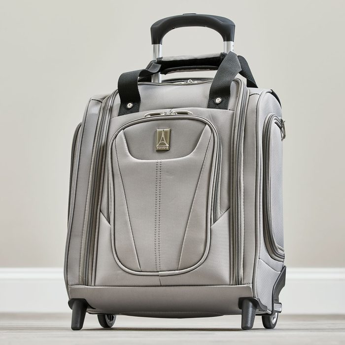 Gray rolling suitcase upright on floor, featuring black handles and zippers, with a logo and stitching details, against a plain wall background.