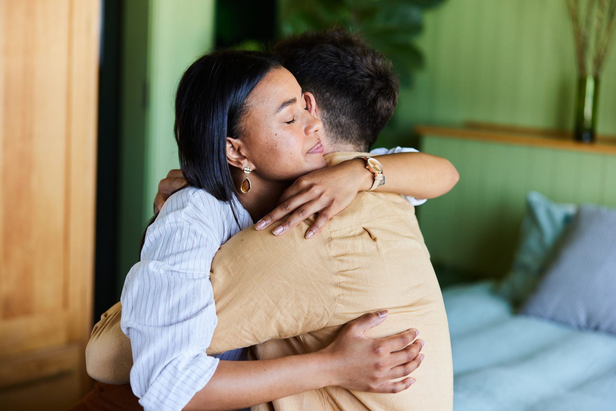 Two people embracing warmly in a cozy room with green walls and soft lighting, conveying a sense of comfort and connection.