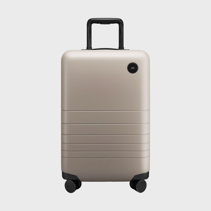 Beige suitcase stands upright on four wheels, featuring a black telescopic handle, in a plain light gray background.