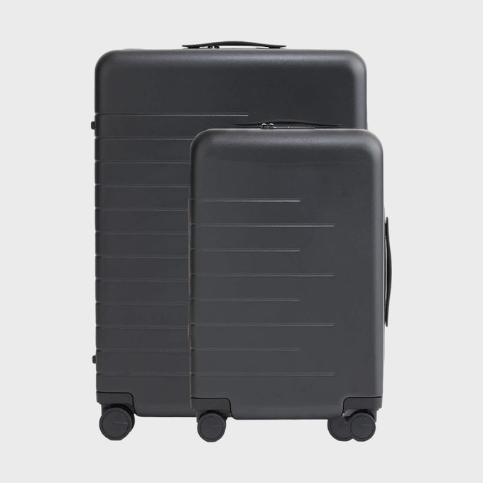 Two dark suitcases stand upright on wheels against a plain background, showcasing their sleek, grooved design.