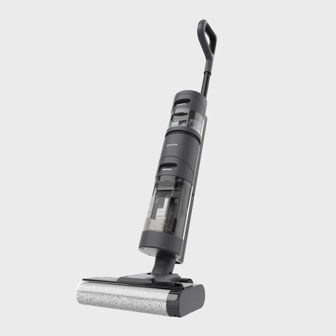 Vacuum cleaner standing upright, handle angled backward, on a plain, light gray background.