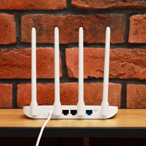 Router with four antennas stands on a wooden shelf against a red brick wall.