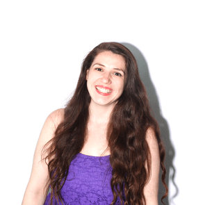A person smiles widely, standing in front of a plain white background, wearing a purple shirt.