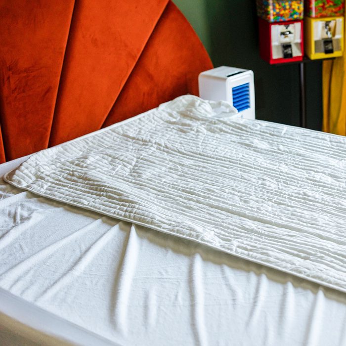White sheet lies flat on a bed with an orange headboard and two candy dispensers nearby.
