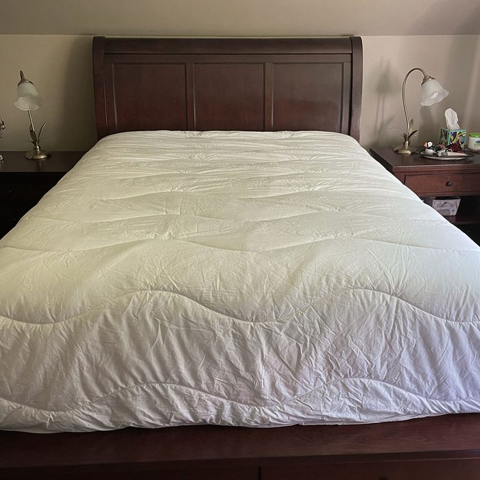 A neatly made bed with a white comforter sits between two nightstands with lamps in a cozy bedroom setting.