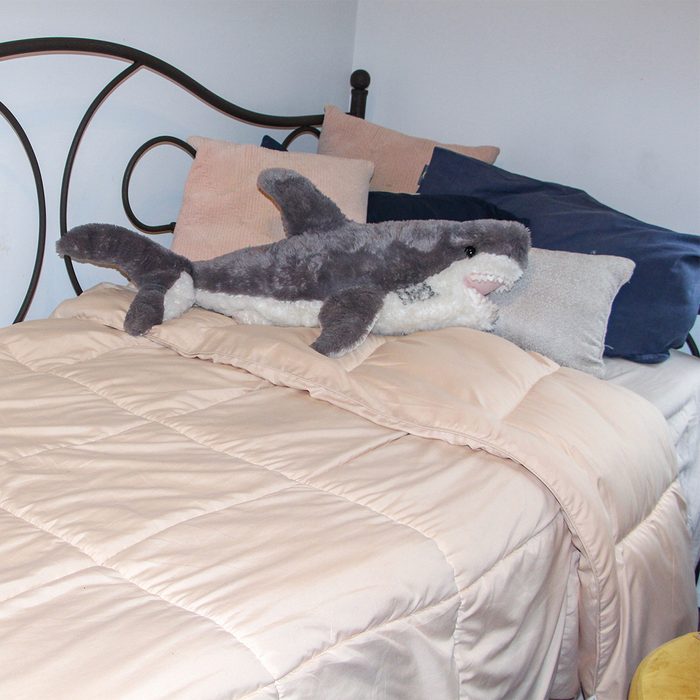 A plush shark rests on a neatly made bed with soft cushions against a decorative metal headboard.