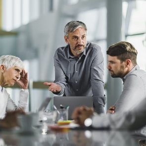 Colleagues discuss actively around a conference table in a modern office setting.