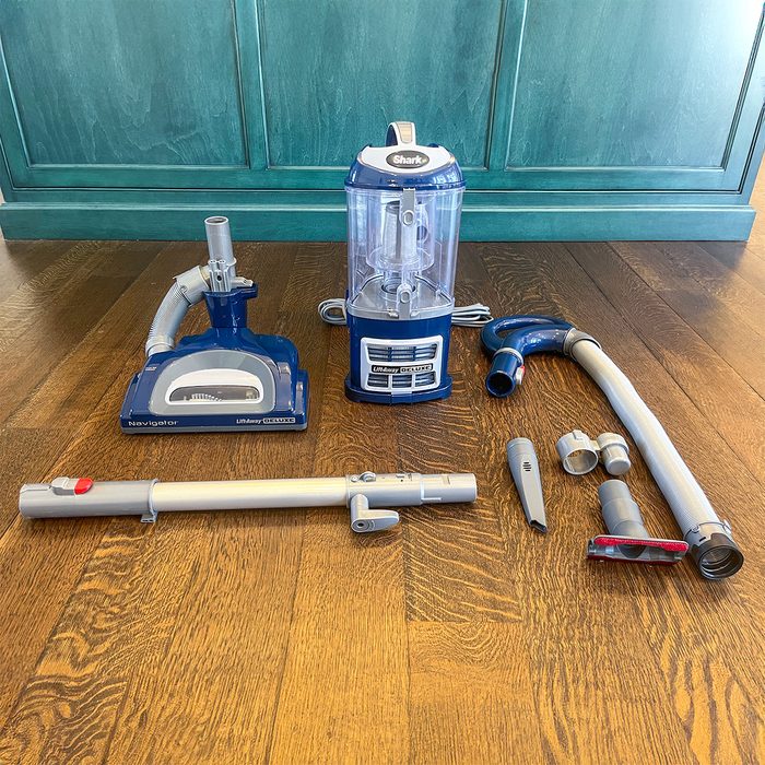 Vacuum cleaner components arranged on wooden floor, with blue and gray parts ready for assembly, near teal cabinet background.