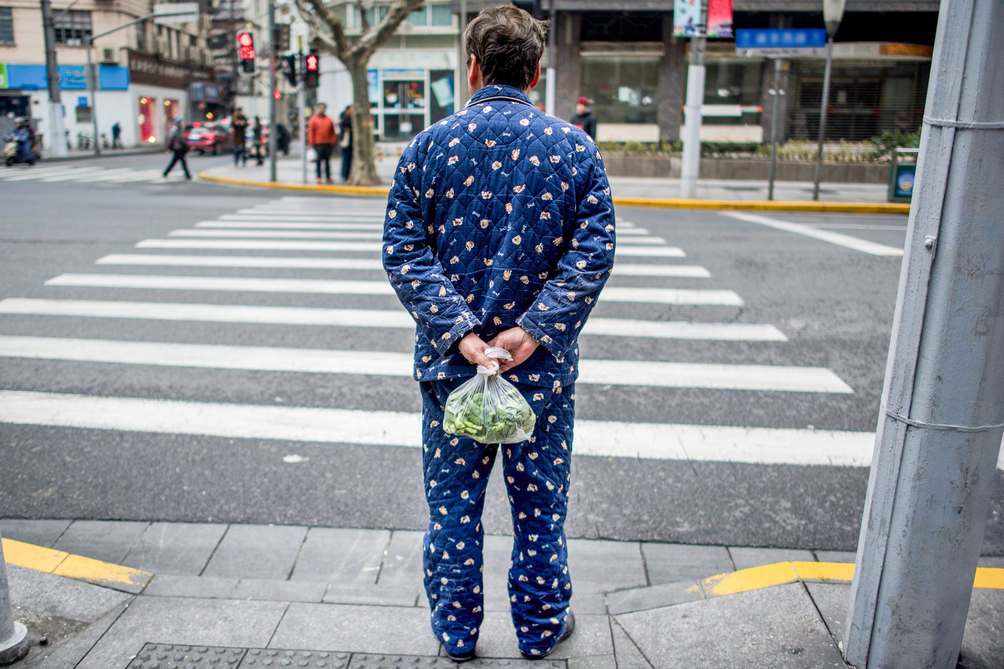 A Man Wearing Pyjamas Carries Vegetables In A Plastic Bag