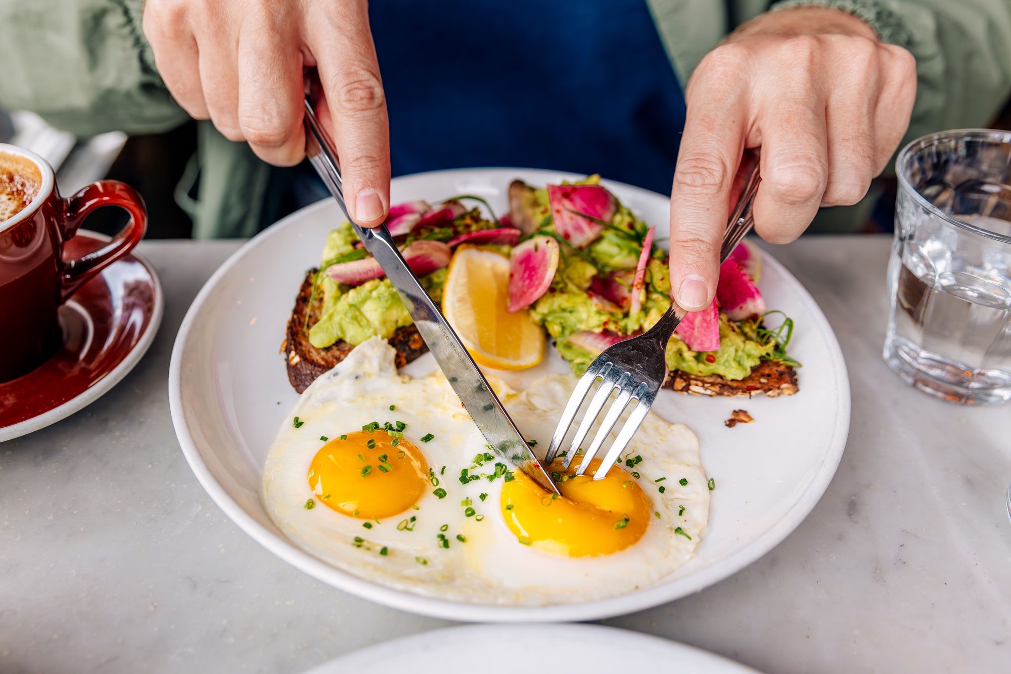 Man Eating Avocado Toast With Sunny Side Up Fried Egg At A Cafe