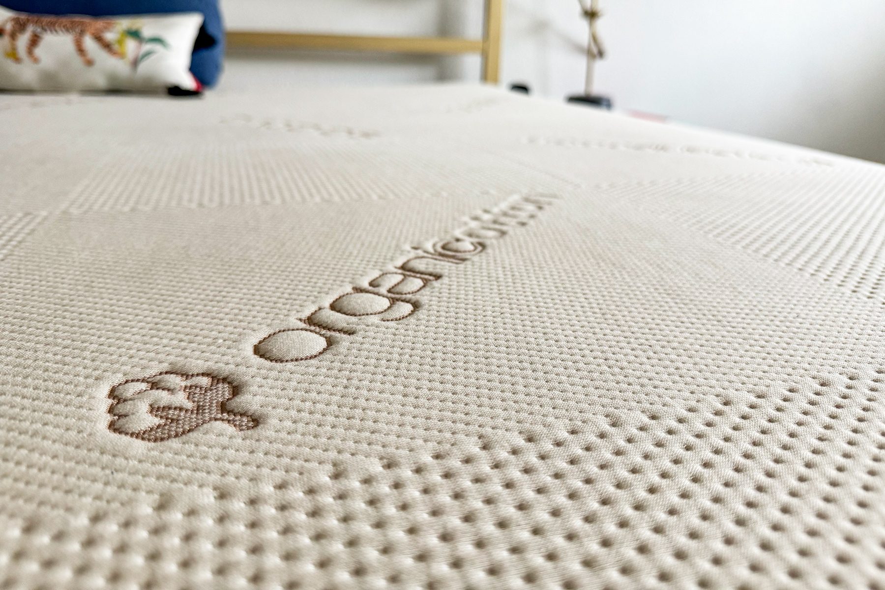 Mattress displays "organiccotton" text; background pillow shows tiger design on bed.