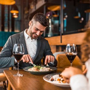 Man dining, cutting food with utensils, surrounded by wine glasses in a stylish restaurant setting.